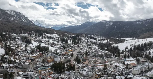 2026 Kış Olimpiyatları için kar kaplı çatılar, alp mimarisi, dağ zirveleri ve inşaat alanlarıyla Cortina dAmpezzo, İtalya 'nın hava manzarası.