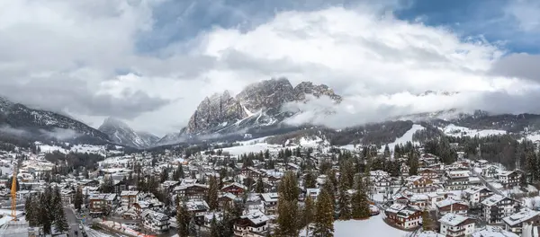 İtalya 'da kar kaplı çatılar, yemyeşil ağaçlar, Dolomitler, alçak bulutlar ve görünür bir vinç ile Cortina dAmpezzo' nun hava görüntüsü.