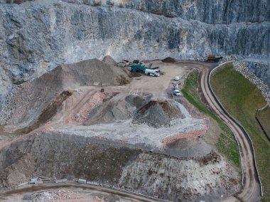 Avusturya Alpleri 'ndeki kazı alanında kamyonlar, makineler, kayalık uçurumlar ve çimenler ve engebeli dağlık arazilerle çevrili toprak bir yol..