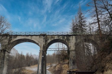 İtalya, Cortina dAmpezzo 'da üç kemerli taş bir viyadük. Karlı zemin, seyrek ağaçlar ve etrafını saran dağlar.
