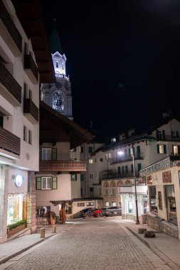 Bazilika 'nın aydınlık çan kulesi Minore dei Santi Filippo e Giacomo, kaldırım taşı caddesi, Alp tarzı binalar ve Cortina dAmpezzo' da hafif ışıklandırma..