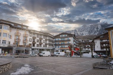 İtalya, Cortina dAmpezzo 'daki büyüleyici kasaba meydanı, dağlık binalar, karlı dağlar ve modern kırmızı ve siyah bir heykel ile çevrili..