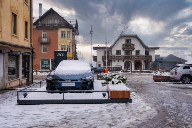Cortina dAmpezzo, İtalya 'da sergilenen Audi e tron GT dörtlüsü, Alp tarzı binalarla çevrili ve kırmızı şemsiyeyle yürüyen bir kişi tarafından karla kaplandı..
