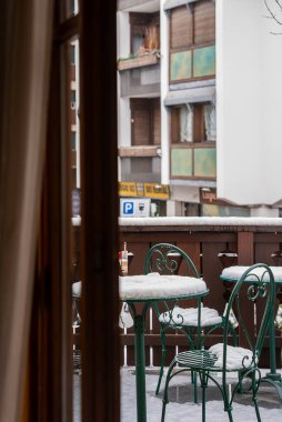 Yeşil işlemeli demir sandalyeli balkon ve karla kaplanmış masa, ahşap korkuluklar ve Cortina, Dolomitler, İtalya 'da çok katlı binalar..