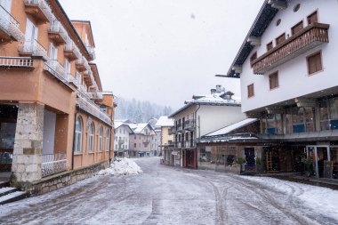 Cortina dAmpezzo, İtalya 'da sessiz bir karlı cadde, Alp tarzı binalar, ahşap balkonlar ve uzak ağaçlar tarafından çerçevelenmiş karla kaplı çatılar.