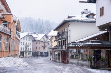 İtalya 'nın Cortina dAmpezzo şehrinde karlı bir caddede, eğimli çatıları ve her yeri yeşil ağaçlarla kaplı dağlık binalar var..