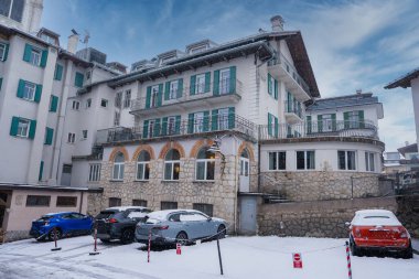 İtalya, Cortina dAmpezzo 'da taş, sıva duvarlar, yeşil kepenkler ve kemerli pencerelerle dolu çok katlı bir bina. Yakınlardaki park halindeki arabaların üzerine kar yağıyor..