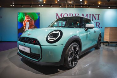 Nane yeşili bir Mini Cooper S, dairesel farları ve kapalı mekanda sergilenen spor ızgarası, daha renkli bir arkaplan ile daha fazla MINI.