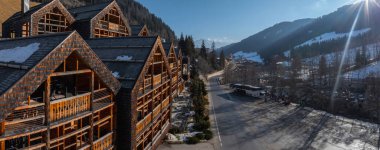 Sarp çatıları olan ahşap dağ evi tarzı bir otel, dolambaçlı bir yolun yanında, karlı ağaçlar, dağlar, bir otobüs ve Dolomitler, İtalya 'da yaşayan insanlar..