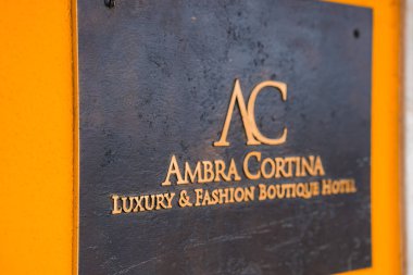 İtalya 'nın Cortina ve Ampezzo kentindeki canlı turuncu bir duvarda Ambra Cortina Lüks ve Moda Butik Oteli için metal tabela..