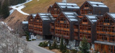 Büyük çok katlı Alp oteli ahşap balkonları, gabayt çatıları ve baca dumanı, Dolomitlerde kar yamaları olan çimli bir yamaçta geçiyor..