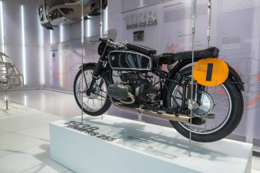 1938 BMW RS 255 motosikleti Münih 'teki BMW Müzesi' nde beyaz bir platformda sergilenmektedir. Siyah bir çerçeve, krom aksanlar ve sarı bir plaka içerir..