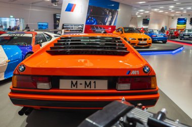 Münih 'teki BMW Müzesi' nde BMW M1 plakalı turuncu BMW M1, diğer canlı BMW modellerle çevrili..