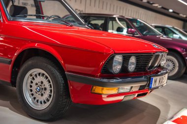 Münih 'teki modern bir müzede, diğer BMW modelleriyle birlikte yuvarlak farları ve krom ızgarası olan canlı kırmızı bir BMW arabası sergilenmektedir..