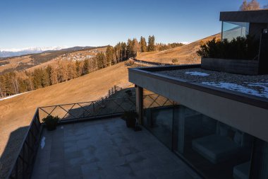 Geniş camlı pencereleri, düz çatısı, fayanslı terası ve tepelere ve Güney Tyrol 'daki karlı dağlara karşı kurulmuş saksı bitkileri olan çağdaş bir otel..