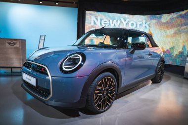 Münih 'teki BMW Müzesi' nde parlak ışık altında sergilenen siyah alaşımlı tekerleri ve LED farları olan metalik mavi bir Mini Cooper..