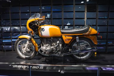 BMW R90S motosiklet turuncu ve siyah dizaynlı, modern yansıtıcı ekran duvarına karşı Münih 'teki BMW Müzesi' nde sergilenmektedir..