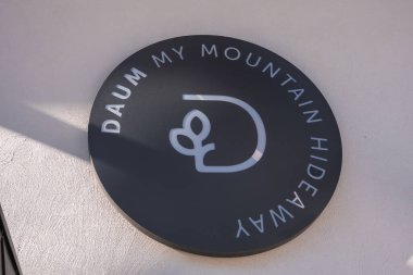 Daire şeklinde siyah bir tabela, muhtemelen Güney Tyrol, İtalya 'da bir ışık duvarına asılmış minimalist logosu olan DAUM My MOUNTAIN HIDEaway yazıyor..