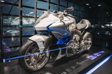 Münih 'teki BMW Müzesi' nde cam bir kutuda parlak gümüş ve mavi bir BMW motosiklet. Bilgi panelleri ve arkaplan gibi modern bir ızgara görünür.