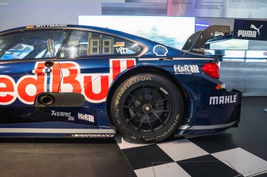 Mavi üniformalı yüksek performanslı BMW yarış arabası, Münih 'teki BMW Müzesi' nin kareli zemininde Red Bull marka ve sponsor logoları sergileniyor..