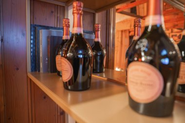 Pembe etiketli ve rafında kitap bulunan temiz düzenlenmiş şarap şişeleri, Cortina, Dolomites, İtalya 'da bir butik otelde sıcak ışıklandırmalı ahşap panellere karşı..