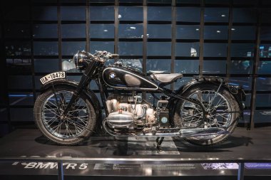 Siyah çerçeveli, krom aksanlı ve BMW logolu klasik bir BMW R5 motosiklet, Almanya 'nın Münih şehrindeki modern koyu renkli bir arka planda sergileniyordu..