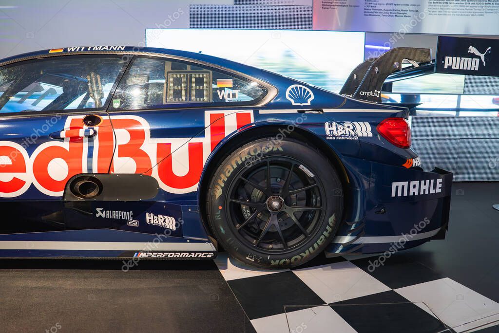 High performance BMW race car with blue livery, Red Bull branding, and sponsor logos displayed on a checkered floor in the BMW Museum, Munich.
