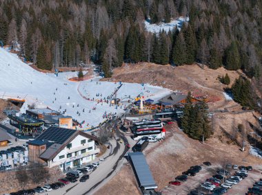İtalya 'nın South Tyrol kentindeki bir kayak merkezinde kar kaplı yamaçlar, Evergreen ormanları, güneş panelli modern binalar ve park halindeki araçlar yer alıyor..