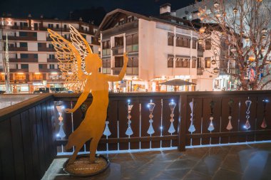 Cortina, Dolomites, İtalya 'daki bir butik otelin balkonunda altın melek heykeli. Alp tarzı binalar ve bir şenlik ağacı görülebilir.