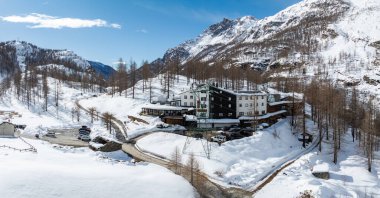 Karla çevrili, karanlık ve beyaz duvarları, seyrek ağaçları ve açık mavi gökyüzünün altındaki Alplerde, Matterhorn yakınlarında engebeli tepeleri olan rahat bir otel..