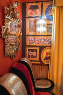 Çerçevelenmiş sanat eserleri, süslü altın aynalar, lüks kırmızı ve altın koltuklar ve İtalya 'nın Cortina kentindeki butik bir otelde sarı bir perde..