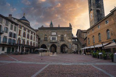 İtalya 'nın Bergamo kentinde bulunan tarihi Piazza Vecchia Meydanı' nda Palazzo della Ragione, Torre Civica, merkezi bir çeşme ve sıcak güneş ışığı altında renkli cepheler yer alıyor..