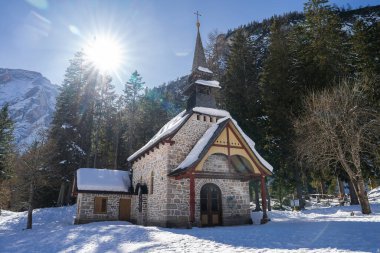 İtalya 'nın Braies Gölü yakınlarındaki karlı bir ormanda sivri uçlu kulesi olan taş bir şapel bulunuyor. Güneş ışığı ağaçların arasından süzülür, arka planda bir dağ zirvesi vardır..