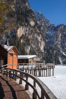 İtalya 'nın Braies Gölü' nde sakin bir kış sahnesi. Kar kaplı kulübeler, ahşap bir iskele, donmuş göl, yemyeşil ağaçlar ve yükselen kayalıklar..