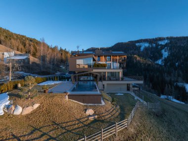 Camdan pencereleri ve ahşap aksanları olan çağdaş bir otel. Alp tepelerine bakan sonsuz bir havuzu, kar tozlu dağları ve açık mavi bir gökyüzü var..