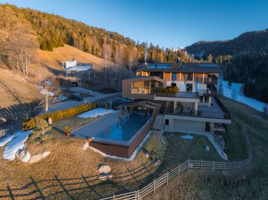 Güney Tyrol, İtalya 'da lüks bir otel. Pürüzsüz tasarım, cam pencereler, teraslar, sonsuz bir havuz, ormanlık tepeler ve karlı arazi manzarası var..