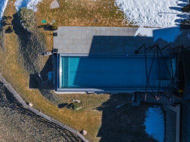 İtalya 'nın Güney Tyrol kentindeki modern bir otelin havadan görünüşü. İçinde kar ve çimenli arazilerle çevrili metal çerçeveli, gösterişli bir açık havuz var..