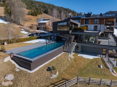 Güney Tyrol, İtalya 'da çağdaş bir otel. Yükseltilmiş sonsuzluk havuzu, ahşap aksanlar, eğimli çatılar ve kar yamalı tepeler var..