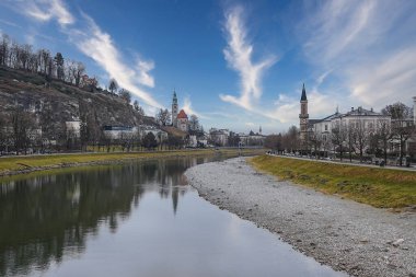 Salzburg, Avusturya manzarası, Salzach Nehri, tarihi binaları olan kayalık bir tepe, bir kilise kulesi, zarif yapılar ve mavi bir gökyüzü..