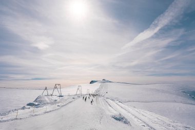 İsviçre 'deki Zermatt kayak merkezindeki karlı alp manzarası, bakımlı bir patikada kayakçılar, kayak kaldırma tesisleri ve güneşli bir tepe noktası.
