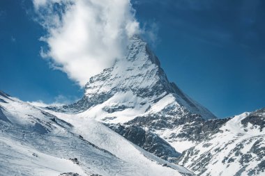 İsviçre, Zermatt yakınlarındaki ikonik Matterhorn dağı, kar kaplı yamaçlar, kayak pistleri, bir kablo kaldırma ve tepemizde parlak mavi bir gökyüzü..