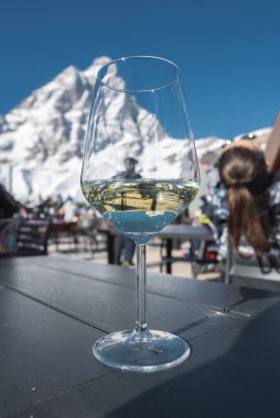 İsviçre, Zermatt 'taki Matterhorn' la açık hava masasında bir bardak beyaz şarap. Kayak ekipmanları ve oturan insanlar açık mavi gökyüzünün altında görülebilir..