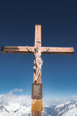 İsa Mesih 'i betimleyen tahta bir haç, kar tepeleri ve açık mavi bir gökyüzü önünde duruyor, muhtemelen Zermatt yakınlarındaki İsviçre Alplerinde..