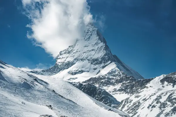 İsviçre, Zermatt yakınlarındaki ikonik Matterhorn dağı, kar kaplı yamaçlar, kayak pistleri, bir kablo kaldırma ve tepemizde parlak mavi bir gökyüzü..