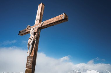 İsa Mesih 'in detaylı ahşap haçı, İsviçre' nin Zermatt kentindeki dağlarla kaplı karla çevrili bulutlu mavi bir gökyüzüne karşı duruyor..