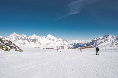 İsviçre 'deki Zermatt kayak merkezinde açık havada kayakçılarla karlı yamaçlar. Matterhorn ve kar kaplı zirveler alp zeminini oluşturur..