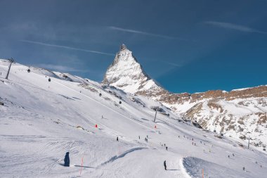 Matterhorn, Zermatt yakınlarındaki İsviçre Alplerinde kar yamaçlarında kayakçılar ve kar kayakçılarıyla berrak mavi gökyüzünün altında yükseliyor..