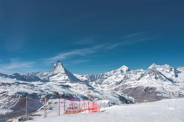 Matterhorn, Zermatt yakınlarındaki İsviçre Alplerinde kar kaplı kayak yamacı, güvenlik ağı ve ön planda kayak kaldırma altyapısı ile belirgin bir şekilde yükselir..