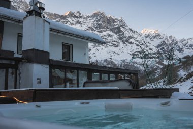Zermatt, İsviçre 'de kar kaplı modern bir otel, ön planda jakuzisi, kayak asansörü yapıları ve yumuşak doğal ışık altında Alpler..