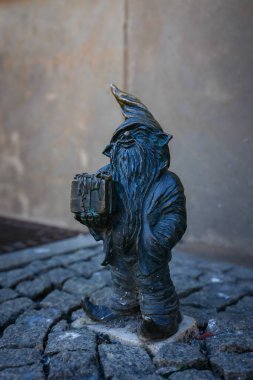 Polonya 'nın Wroclaw şehrinde uzun sakallı ve sivri uçlu küçük bir bronz cüce heykeli düz bir duvara karşı bir hediye kutusu tutuyordu..